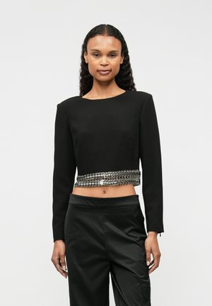 Sort, kortærmet top med lange ærmer, der har en sølvkædeaccent ved taljen. Stoffet er glat med en struktureret pasform og en rund halsudskæring.