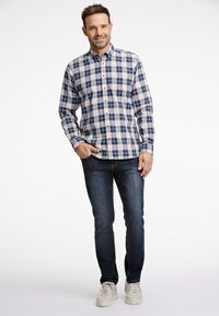Camisa de botones con un patrón de cuadros en azul, blanco y naranja, hecha de algodón, combinada con jeans de mezclilla oscura y zapatillas blancas.