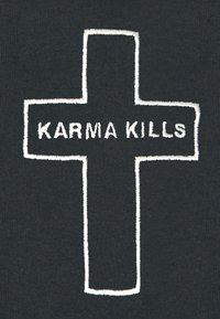 Črn material z izstopajočim belim vezom prečnim dizajnom, ki vključuje besedilo "KARMA UBIVA" v strukturo križa.