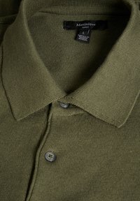 Olivově zelený pletený polo shirt s límečkem a dvěma knoflíky, s černou cedulkou s nápisem "Matinique Europe" a velikostí L.