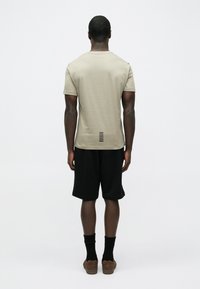 Beež lühikeste varrukatega t-särk tavalise lõikega, näidatud tagantpoolt, millel on tekstuuriga disain ja vertikaalsed mustad triibud ääre lähedal.