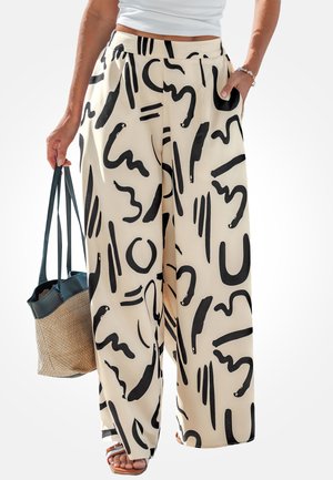 Beige wijde broek met gedurfde zwarte abstracte penseelstreekpatronen, gecombineerd met een wit topje, sandalen en een geweven draagtas.
