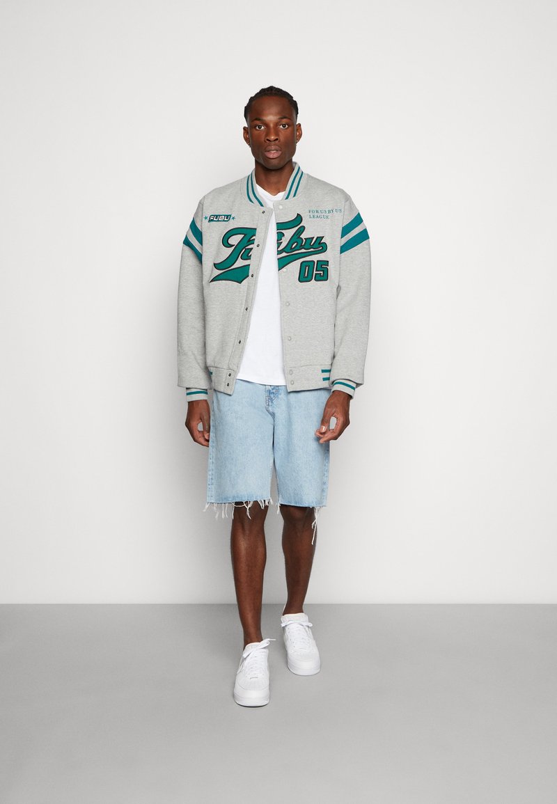 Gray varsity jacket with teal accents, front buttons, and graphic lettering, paired with light blue denim shorts and white sneakers.