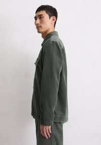 Zielona kurtka ze sztruksu z kołnierzem, pojedynczą kieszenią na piersi i mankietami na guziki. Tkanina ma pr�ążkowaną fakturę, która pasuje do dopasowanych spodni.