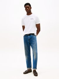 White short-sleeve t-shirt with logo, paired with blue straight-leg jeans featuring a faded finish. Dark loafers with tassels.