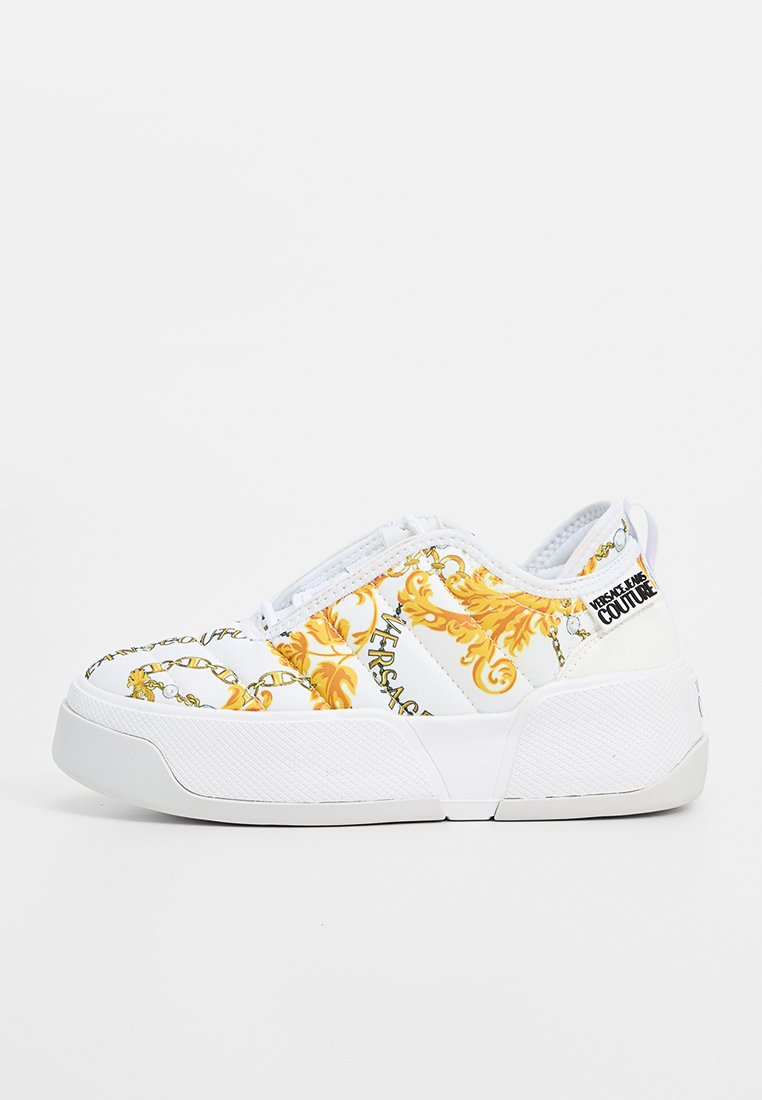 Weiße Sneaker mit gelbem Barockmuster, strukturierten Seiten und einer klobigen weißen Sohle. Mit Logodetails an Ferse und Schnürsenkeln.