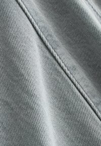 Gros plan sur un tissu tricoté gris clair montrant un tissage détaillé et une couture centrale en relief traversant en diagonale.