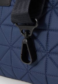 Granatowa torba pikowana z czarnym metalowym klipsem, teksturowanym materiałem i mocnym paskiem z diagonalnym wzorem. 