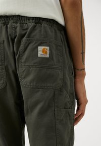 Donkergroene cargobroeken van duurzaam stof, met een elastische tailleband en meerdere zakken, met een Carhartt-logo patch op de achterzak.