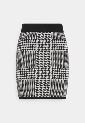 Mustavalkoinen houndstooth-neulehame geometrisella tilkkutyökuviolla, vartalonmyötäinen siluetti sekä musta elastinen vyötärönauha ja helma.
