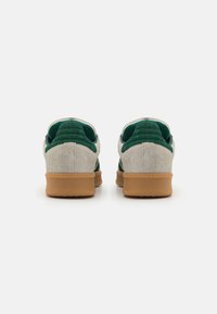 Baskets en suède vert et beige avec une semelle en gomme, dotées d'un col rembourré et d'accents texturés au niveau du talon. Vue arrière.