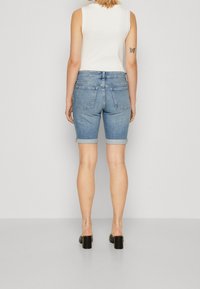 Vaaleansinisen pesun farkkushortsit, joissa on käännetty helma, kaksi takataskua ja istuva vyötärönauha, yhdistetty valkoiseen hihattomaan toppiin.