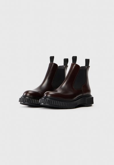 Botine Chelsea din piele maro, cu panouri elastice laterale, vârf rotund și o talpă din cauciuc negru, groasă, cu strieri texturate.