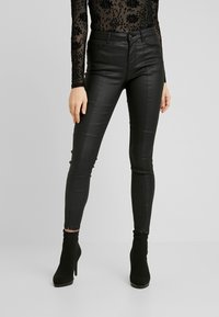 Pantalones skinnies de piel sintética negra con una textura suave, cintura alta y cremallera frontal. Combinados con botas de tobillo negras para un look elegante.