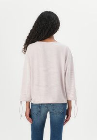 Lyse rosa stripete genser med trekvart ermer, med knytte-detaljer ved mansjettene. Kombinert med blå jeans for en avslappet stil.