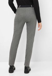 Pantaloni su misura grigi con taglio dritto, tessuto strutturato e cintura scura. Stivaletti neri completano l'outfit.