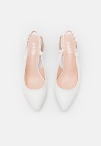 Talons hauts slingbacks blancs avec un bout pointu, un design avec des découpes sur les côtés et une semelle intérieure beige. Présente une fermeture à boucle et une texture lisse.