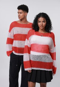 Due modelli indossano maglioni in maglia oversize con strisce orizzontali rosse e bianche. La trama è leggera e uno dei modelli abbina il proprio a pantaloni neri.