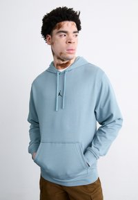 Sudadera azul claro hecha de un tejido suave, con bolsillo delantero, cordones ajustables y un logo negro en el pecho.