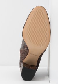 Chaussure en cuir marron texturée avec bout pointu, semelle striée, talon bloc, et logo ALDO au centre de la semelle.