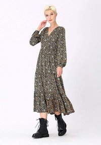 Robe longue à manches longues avec un col en V, fond noir, motifs crème et dorés. Associée à des bottes de combat noires à lacets. Jupe fluide.