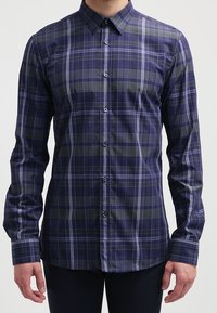 Camisa de cuadros azul marino con mangas largas, cuello abotonado y botones blancos. Presenta franjas en verde oscuro y gris claro en un patrón de cuadros.