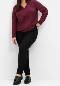 Långärmad blus i burgundy med geometriskt mönster, V-ringning och svarta slim-fit byxor. Svarta loafers med fransdetalj fulländar outfiten.