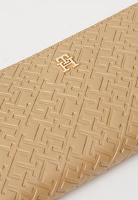 Beige, textúrált bőrtáska, amely kiemelkedő geometrikus mintázattal és arany logós díszítéssel rendelkezik. Simább felületű, strukturált formájú.