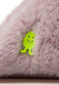 Zapatilla suave y esponjosa de color rosa que presenta una superficie texturizada y un detalle de un personaje sonriente en un vibrante color verde. El diseño enfatiza la suavidad y la comodidad.