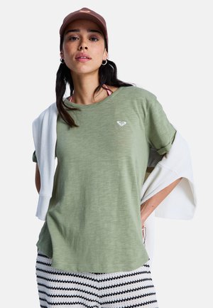 Groene katoenen t-shirt met korte mouwen, ronde halslijn en wit logo op de borst. Gecombineerd met gestreepte zwart-witte broeken en een witte trui.