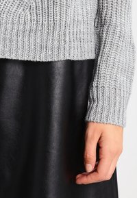 Maglione grigio a maglia con una trama a coste, abbinato a una gonna nera in pelle liscia, messo in mostra nei polsini e nell'orlo.
