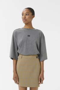 T-shirt gris oversize avec des manches larges, arborant un petit logo noir, associé à une mini-jupe à carreaux jaunes avec un détail de bouton.
