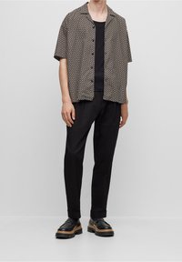 Camisa de manga corta con estampado en marrón y crema, con un corte relajado, combinada con pantalones negros y zapatos negros gruesos con suela marrón.
