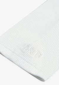 Bela ribasta tkanina z mehkega materiala, ki ima reliefno podrobnost logotipa. Rob ima čisto, šivano obdelavo.