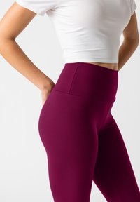 Hoge taille leggings in diep bordeaux, gemaakt van rekbare stof. Gladde textuur zonder zichtbare patronen of hardwaredetails.