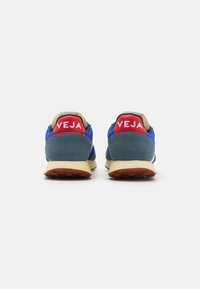 Blue and green sneakers with a beige sole, featuring red heel tabs with "VEJA" logo, textured fabric upper, and rubber outsole with tread.