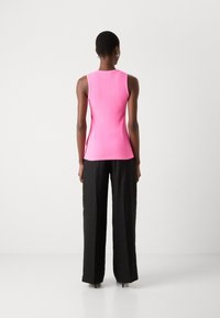 Tett rosa ribbestrikket tanktop, ermeless design, kombinert med løse svarte bukser. Glatt tekstur, uten synlige mønstre eller accenter.