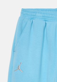 Gaiši zila elastīga josta sporta bikses ar sānu kabatu un sudraba Jumpman logo izšuvuma tuvumā kabatai.