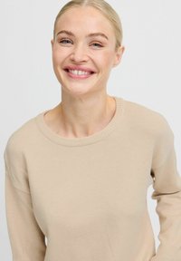Maglione beige a maglia con scollatura rotonda e maniche lunghe. Texture liscia con rifiniture a coste sui bordi del colletto, dei polsini e dell'orlo.