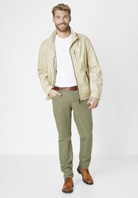 Beige lightweight jacket with zip and pockets, white t-shirt, olive green pants, brown leather belt, and brown lace-up boots.
