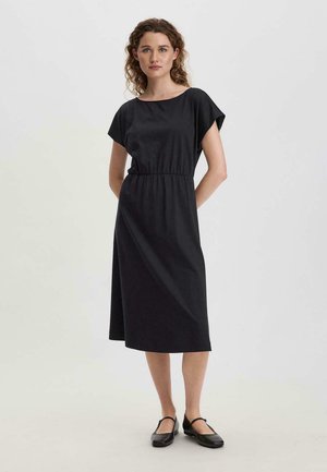 Zwarte katoenen jurk met korte mouwen, ronde hals en elastische taille. Valt tot onder de knie. Gekocht met zwarte platte schoenen.