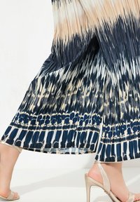 Plisserad maxiklänning med ett gradientmönster som övergår från krämfärgad till marinblå. Tyget är lätt och har en slät textur med en kontrasterande fåll.