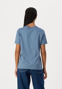 Camiseta de algodón azul con mangas cortas, cuello redondo y ajuste relajado. Llevada con unos vaqueros de mezclilla de tiro alto y corte holgado.