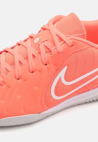 Korálově růžová sportovní obuv vyrobená z prodyšné síťoviny a syntetického materiálu s texturovanými akcenty, která má bílé tkaničky a bílé logo.