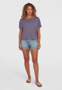 Lilla kortærmet T-shirt med tekstureret logo, parret med lyseblå denimshorts og hvide flip-flops. Casual, afslappet pasform.
