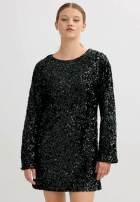 Vestido negro de lentejuelas con mangas largas, cuello redondo y corte holgado. Textura brillante gracias a las lentejuelas dispuestas densamente sobre una tela suave.