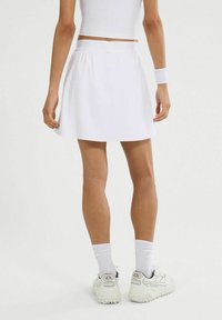 Weißer Sportrock mit glatter Textur und elastischem Bund, kombiniert mit weißen Socken und Turnschuhen. Schlichtes Design, keine Muster.