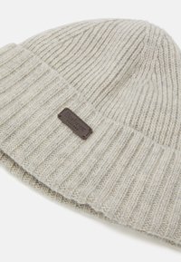 Crème gebreide beanie muts met ribbelstructuur, voorzien van een donkerbruin leren logo-label. Zacht, warm materiaal, geschikt voor koud weer.