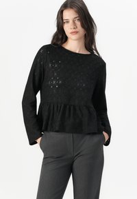Maglione nero con texture, maniche lunghe, scollatura rotonda e orlo a peplum. Presenta un motivo sottile e dettagli intricati.
