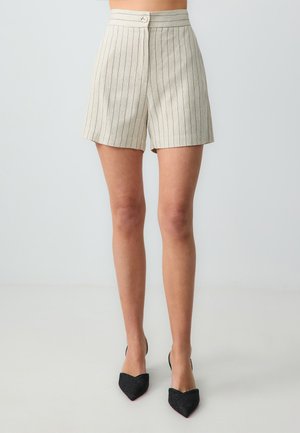 Pantaloni corti beige con strisce verticali blu scuro, vita alta, chiusura a bottone e vestibilità su misura, abbinati a tacchi a punta neri.